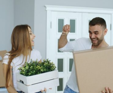 Person sits on the floor of an empty room, surrounded by packed cardboard moving boxes, looking thoughtful about the movin...