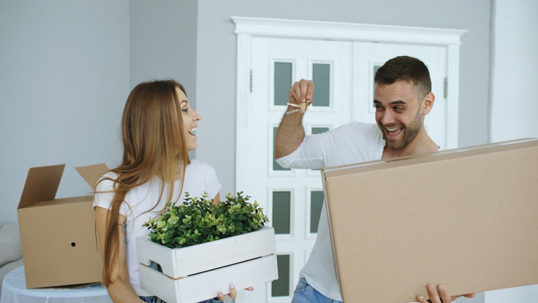 Person sits on the floor of an empty room, surrounded by packed cardboard moving boxes, looking thoughtful about the movin...