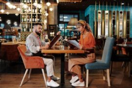 Person in a dimly lit, stylish restaurant is intently studying a menu, their face highlighted by dramatic lighting, convey...